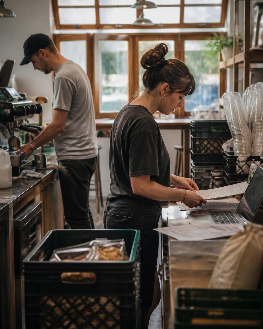Café team working behind the counter with supplies, invoices, and a laptop